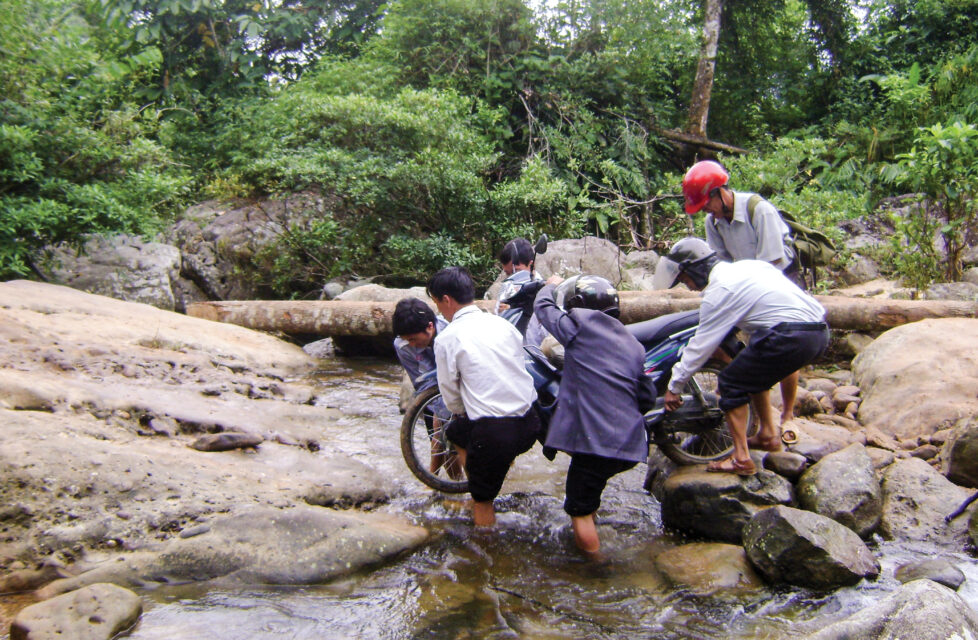 Front Line Workers Refuse Commands to Stop Preaching men help carry motorcycle across stream