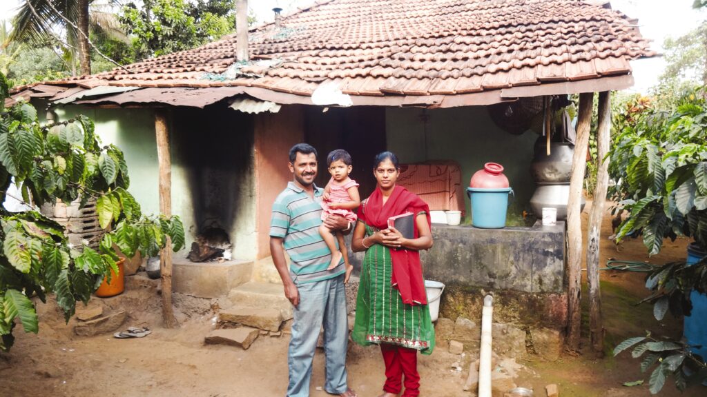 Chandrashekar stands outside his home with his wife and child