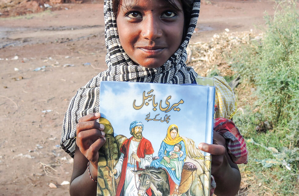 Child stands holding a bible and smiling