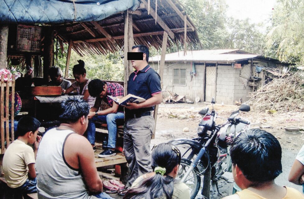 Former Islamic Terrorist Now a Faithful Pastor a man reads the bible to a group of men outside in their village