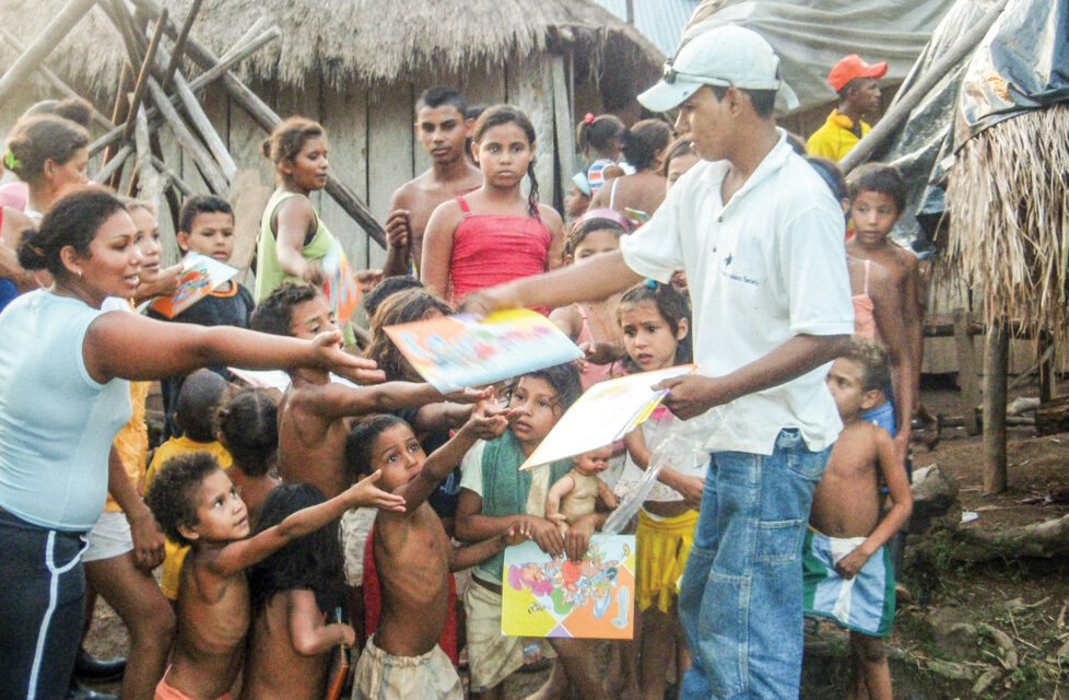 Child Survives FARC Attack, Becomes Red-Zone Pastor Boy hands out book to children in a village